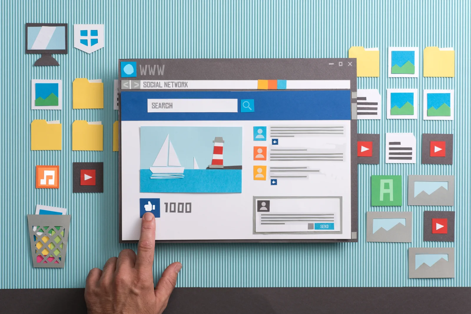 Aus Papier geschnittenes Browserfenster eines sozialen Netzwerks, ein Finger drückt den Gefällt-mir-Knopf, ringsum Symbole für Bilder, Musik und Video
