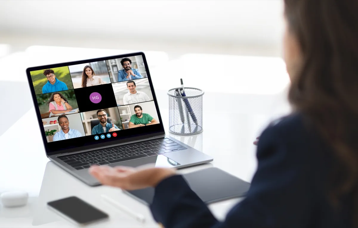 Eine Frau sitzt vor einem Laptop mit einer Videokonferenz aus neun Teilnehmerkacheln